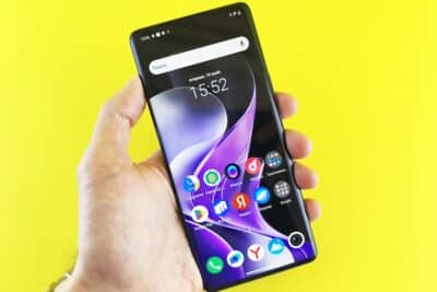 Close-up of a hand holding a smartphone on a bright yellow background.