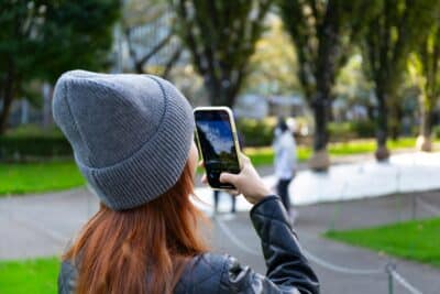 Young woman in Tokyo's Minato City capturing park scenery with her smartphone on a sunny day.