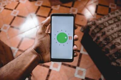 Close-up of a hand holding a smartphone displaying Android 11 interface indoors on patterned floor.
